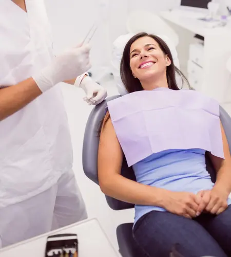 Mujer sonriente sentada en el sillón dental conversando con un odontólogo con uniforme blanco y guantes.